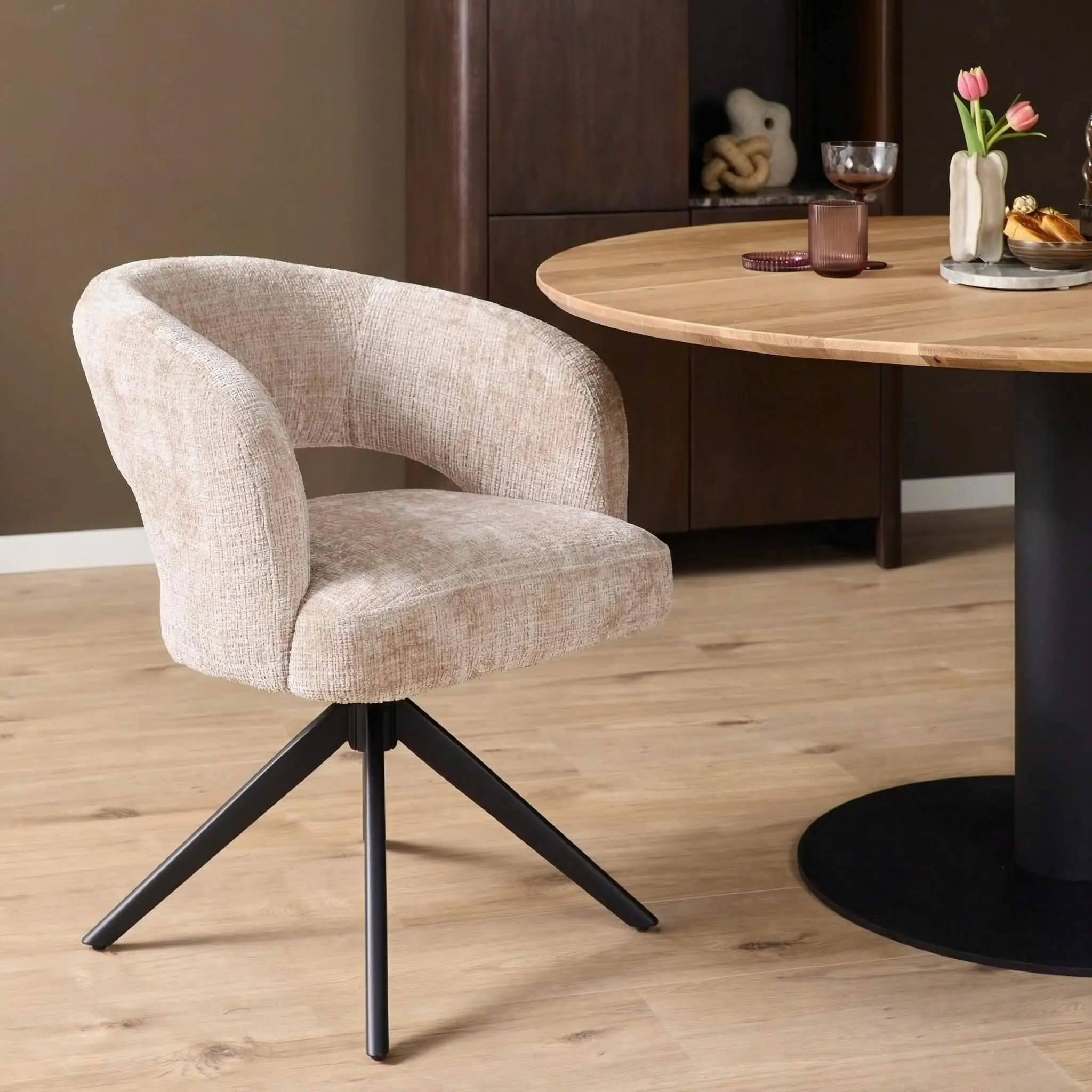 Draaibare armstoel Demi in beige stof met zwart metalen onderstel aan ronde eettafel