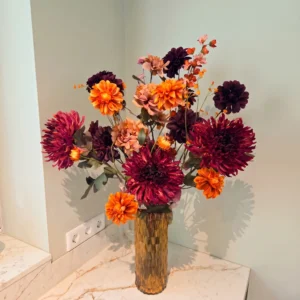 Groot herfstboeket in bordeauxrood, warm oranje en zalmroze in glazen vaas